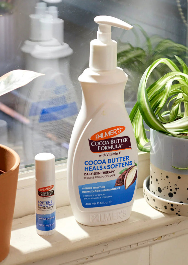Palmer's Cocoa Butter Formula bottle and stick on a windowsill with plants in the background