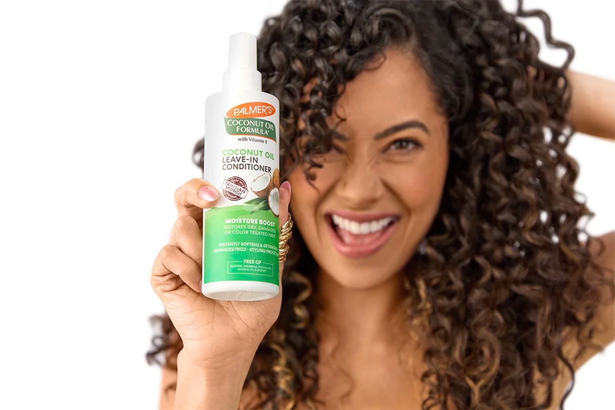 Woman holding a Palmer's Coconut Oil Formula leave-in conditioner bottle with a white background