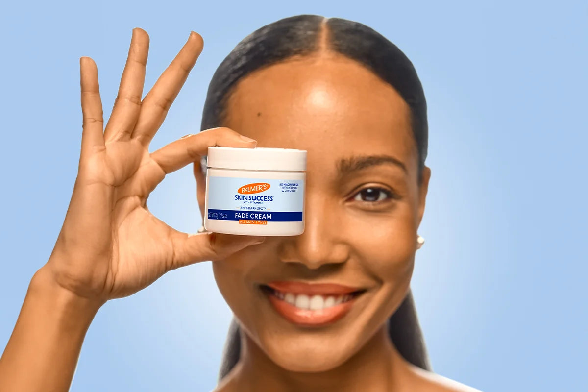 Woman holding a jar of Vaseline face cream against a clear blue sky